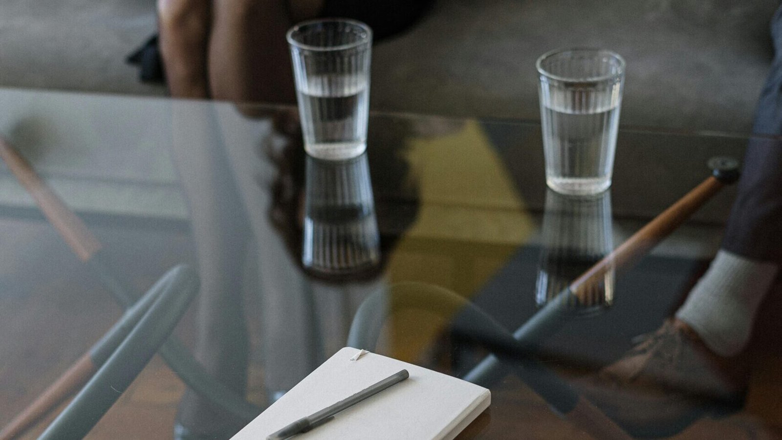 Close-up of a counseling session with two glasses of water and a notepad on a glass table.